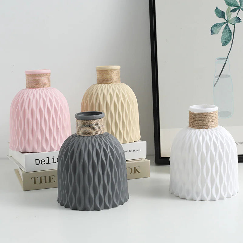 Four ceramic vases in pink, beige, gray, and white on a light surface with books in the background.