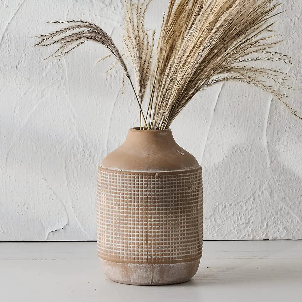 Textured ceramic vase with dried grasses against a white wall