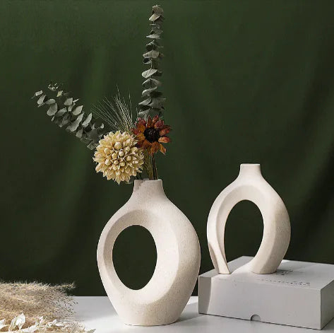 Two white ceramic vases with circular designs on a dark green background