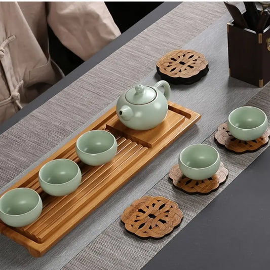 Tea set with green teapot and cups on a wooden tray on a gray surface.
