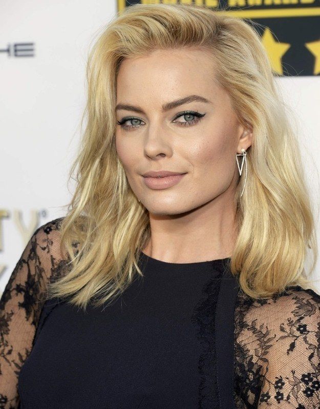 Woman with blonde hair and tattoos on arms wearing a black lace top.